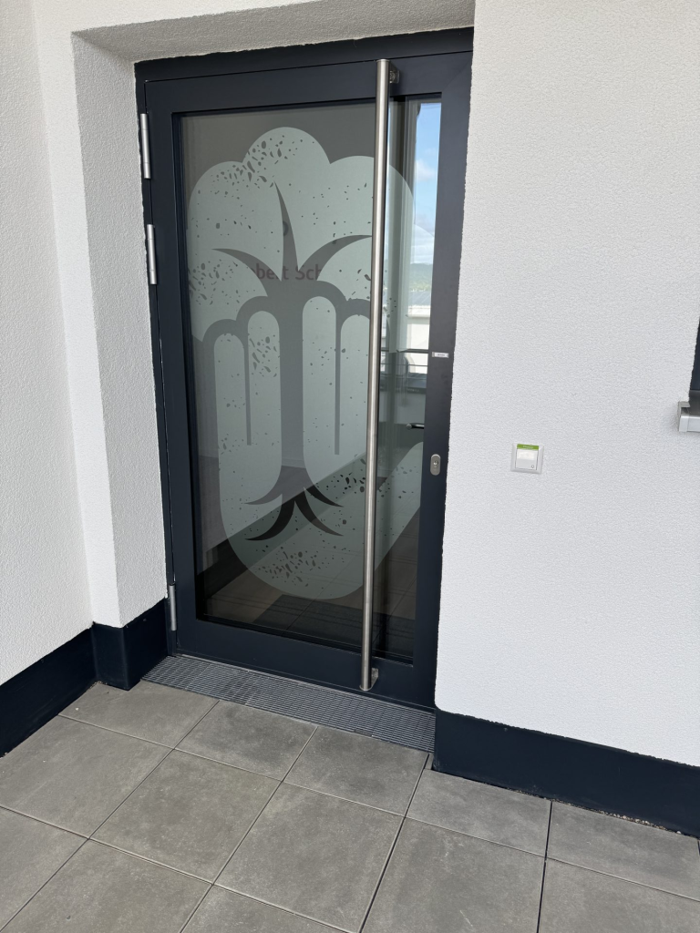 Physiotherapie-Raum mit hellgrüner Behandlungsliege, Kettlebells, Hanteln und großem Fenster mit Blick auf grüne Hügel.